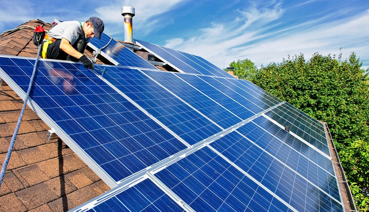 Homem fazendo a instalação dos painéis de energia solar em telhado de residência 