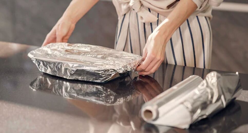 Dona de casa envolvendo sua travessa de alimento com papel alumínio