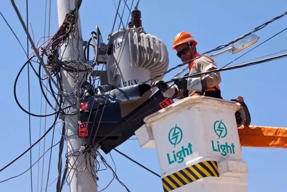 No alto do poste de rua, funcionário da companhia de energia elétrica da Light faz reparos (Fotos: Reprodução/ Light/ Internet)