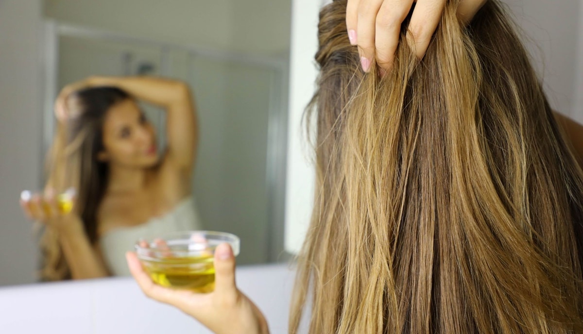 Mulher aplicando azeite nos cabelos para melhor saúde capilar (Foto: Reprodução/ FreePik)